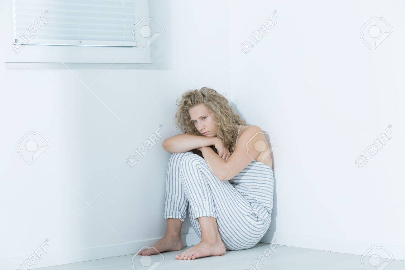65999858-Mental-hospital-patient-sitting-on-a-floor-in-a-white-room-Stock-Photo